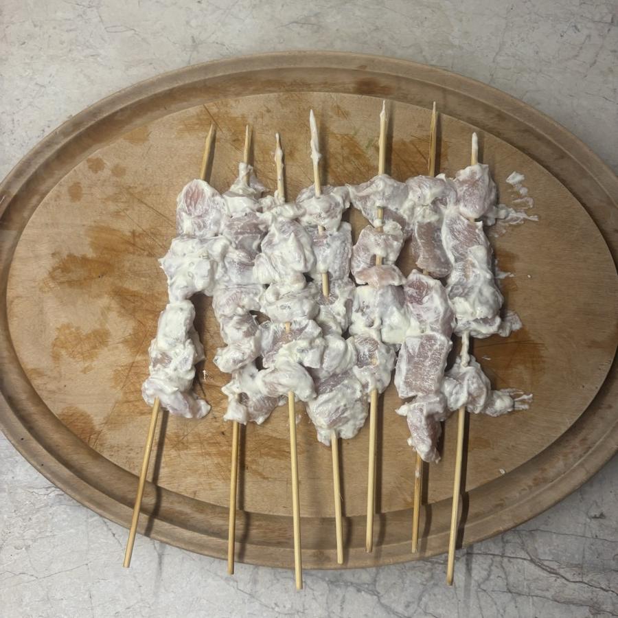Rohe Pouletspiesse in der Joghurtmarinade auf einem Holzbrett, bereit für den Grill